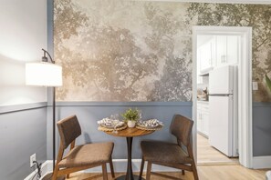 A dining area with two chairs, a table, a lamp, and a wall with a tree mural.