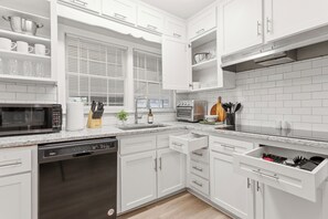Una cocina moderna con armarios blancos, horno integrado, microondas y lavavajillas.