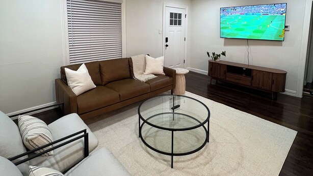 Una sala de estar moderna con un sofá marrón, una mesa de centro de vidrio y un televisor montado en la pared.
