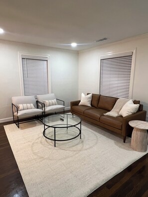 A living room with a brown sofa, two armchairs, a glass coffee table, and a small side table. - Renovated 2BR in Irving - King Bed (Irving)
