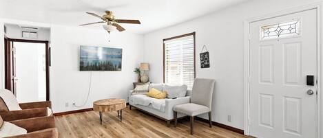 A living room with a ceiling fan, a sofa, a chair, a coffee table, and a television.