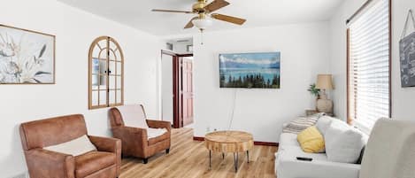 A living room with a ceiling fan, a sofa, two armchairs, a coffee table, and a painting on the wall.