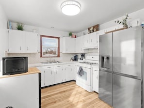A modern kitchen with white cabinets, stainless steel appliances, a wooden countertop, and a window with blinds. - Pet-Friendly 4BR - Free Parking - Utah Retreat (West Valley City)