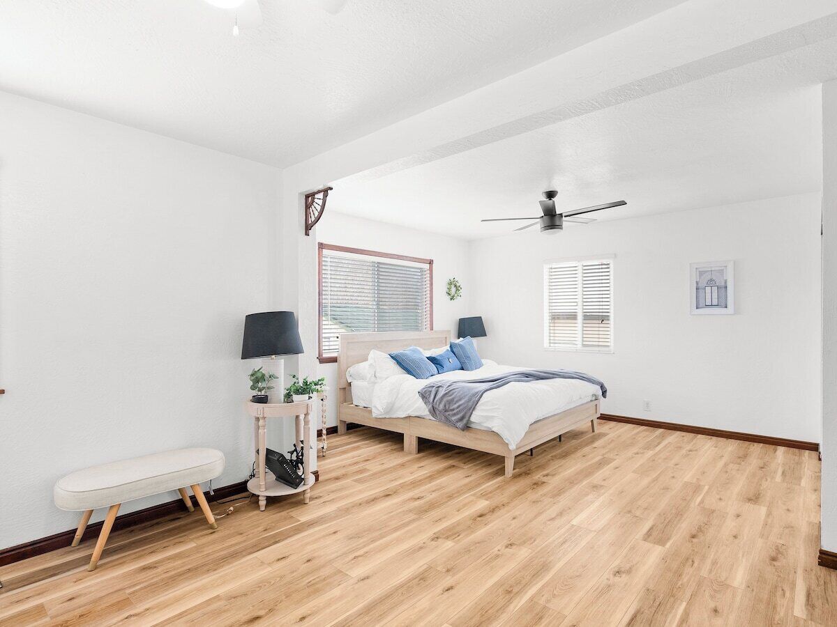 Ein Schlafzimmer mit Bett, Nachttischen, einer Bank, einem Deckenventilator und einem Fenster mit Jalousien.