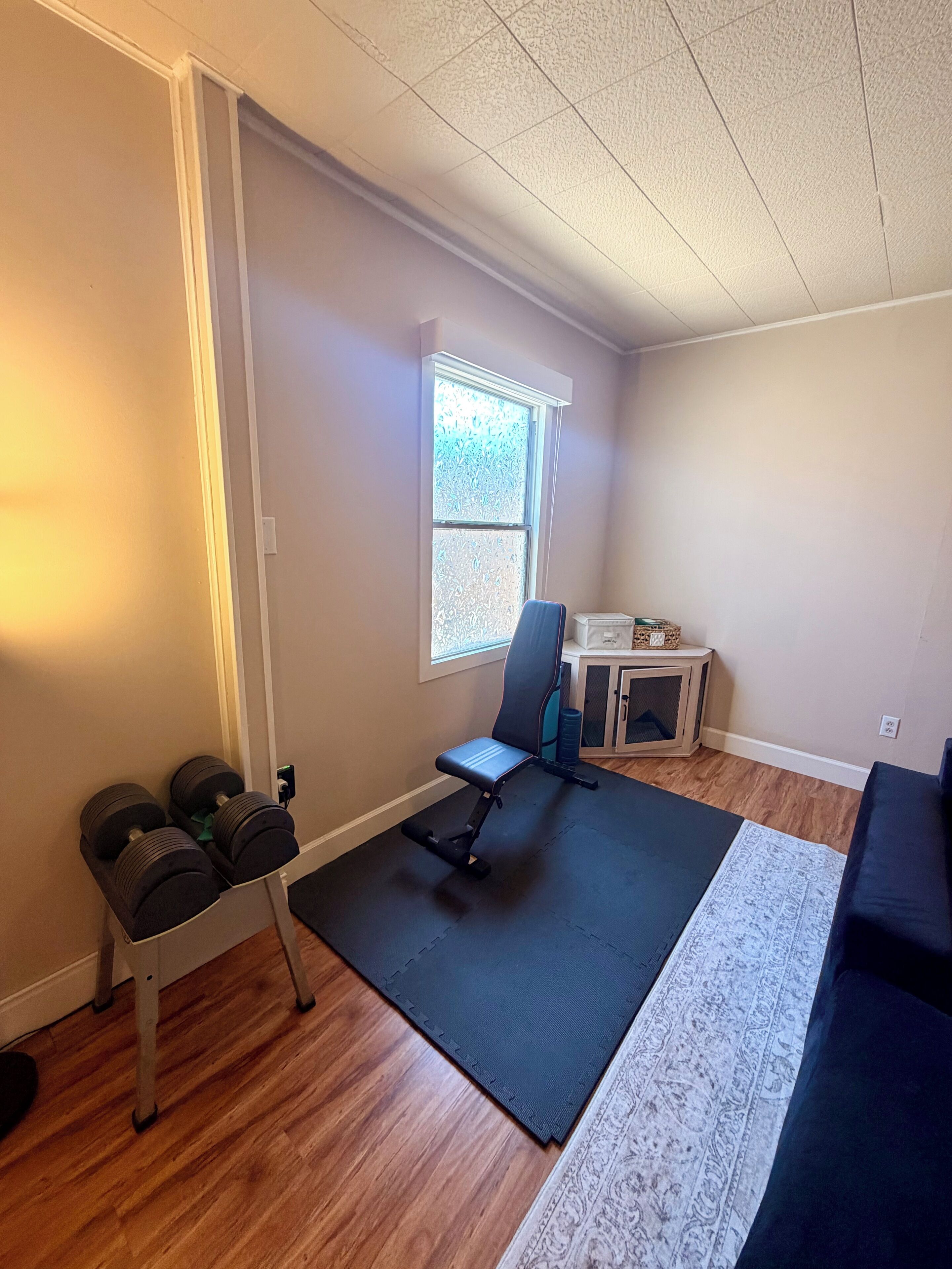 Habitación con zona de ejercicio que incluye mancuernas, una silla y una colchoneta.