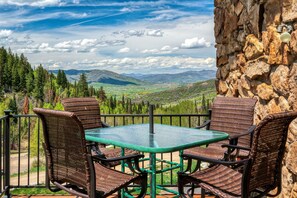 A terrace with a glass table and wicker chairs, overlooking a mountainous landscape.