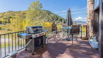 Una terraza exterior con una parrilla, una mesa con sillas y vistas a un paisaje montañoso.