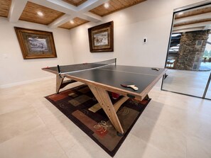 Una mesa de ping pong en una habitación con vigas de madera en el techo, cuadros en la pared y un pilar de piedra.