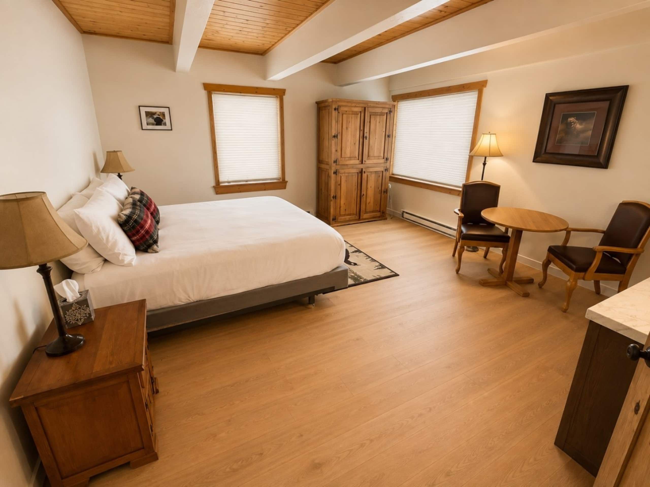 Ein Schlafzimmer mit einem Bett, Nachttischen, einem Sessel, einem kleinen Tisch und einem Kleiderschrank.
