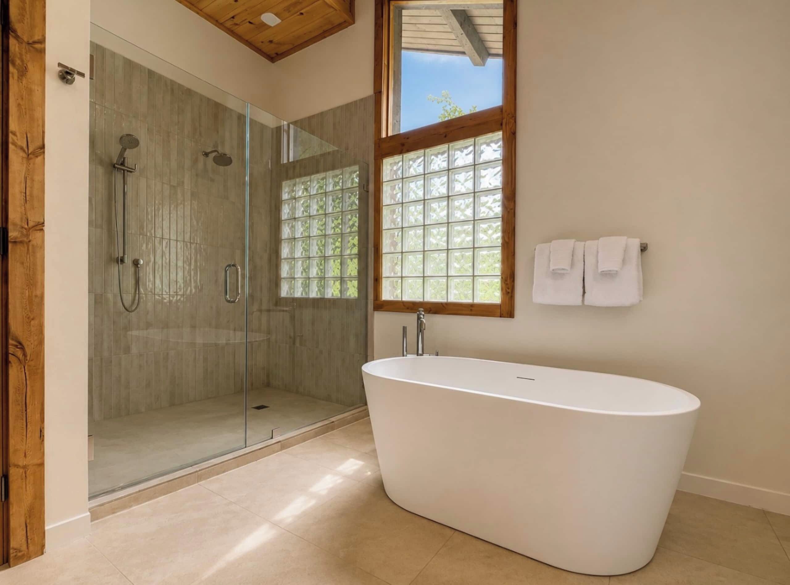 A modern bathroom with a glass-enclosed shower, a freestanding bathtub, and a window with a view.