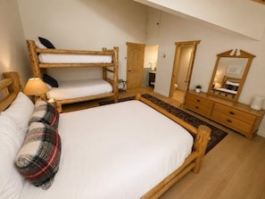 A room with a bunk bed, a single bed, a dresser, a mirror, and a lamp.