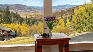 Una mesa de madera con una cámara y flores, con vistas a un paisaje montañoso con follaje otoñal.