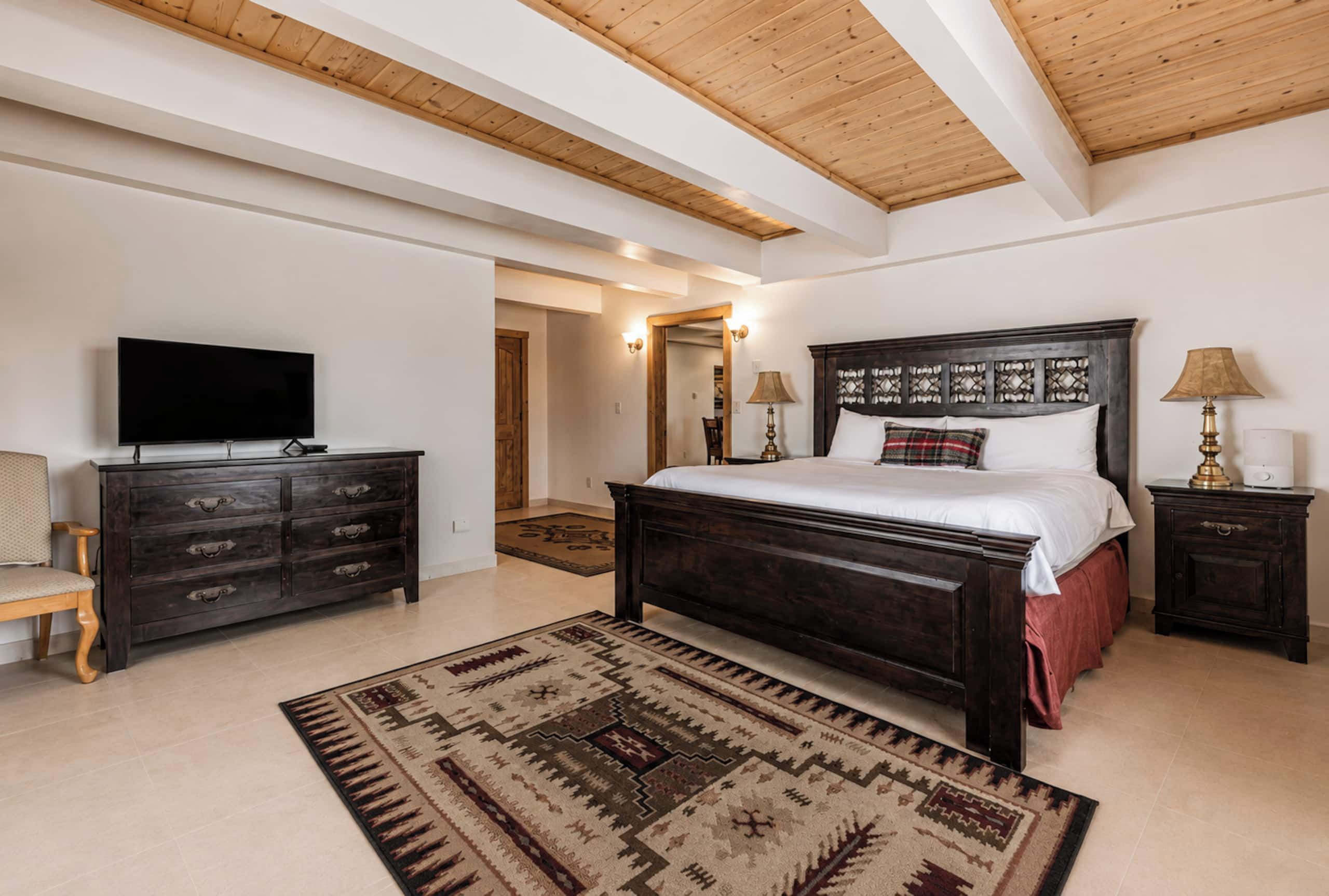 Un dormitorio con una cama grande, televisor, cómoda y alfombra.