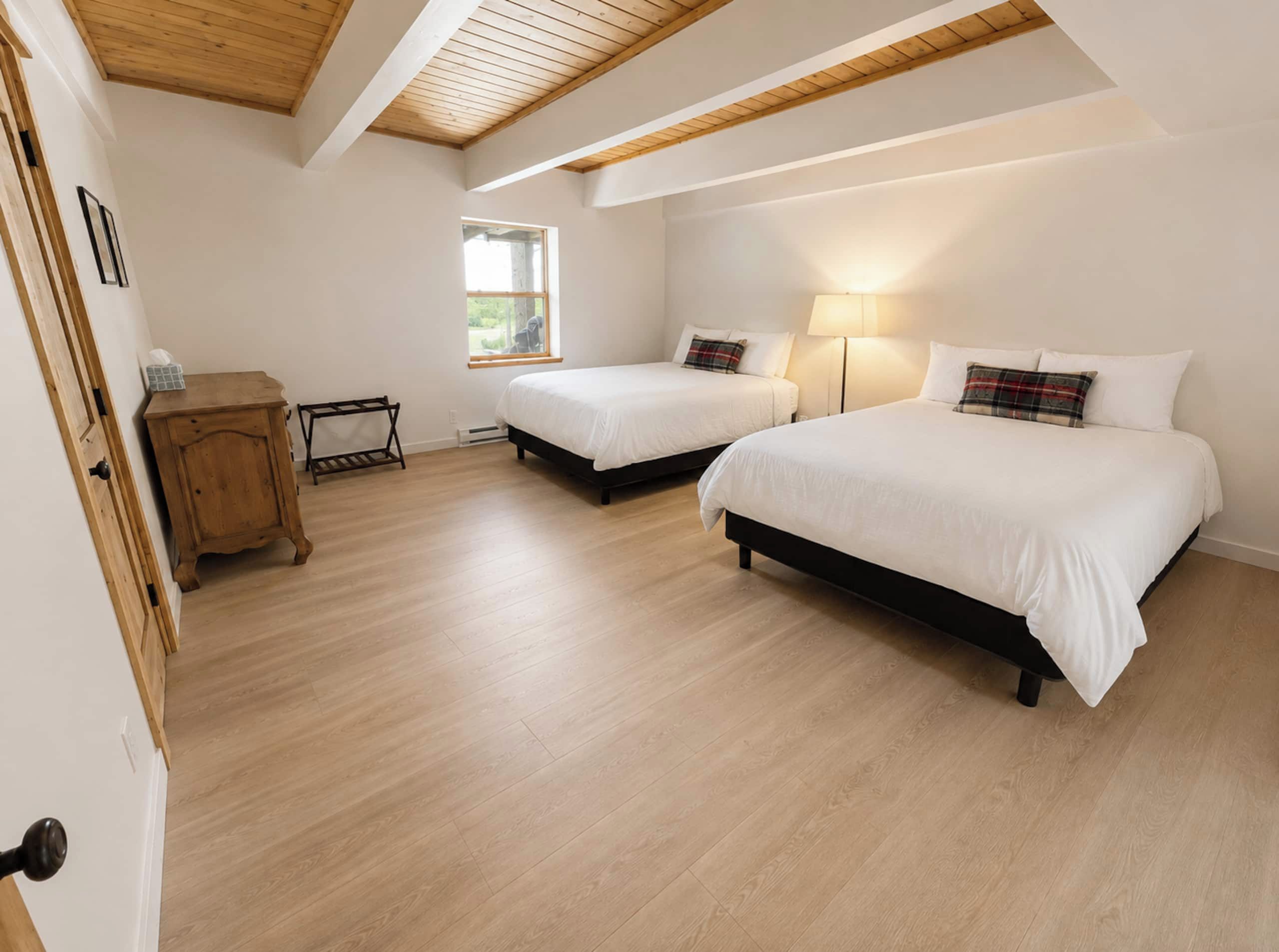 A bedroom with two beds, a wooden cabinet, a window, and a ceiling with exposed beams.