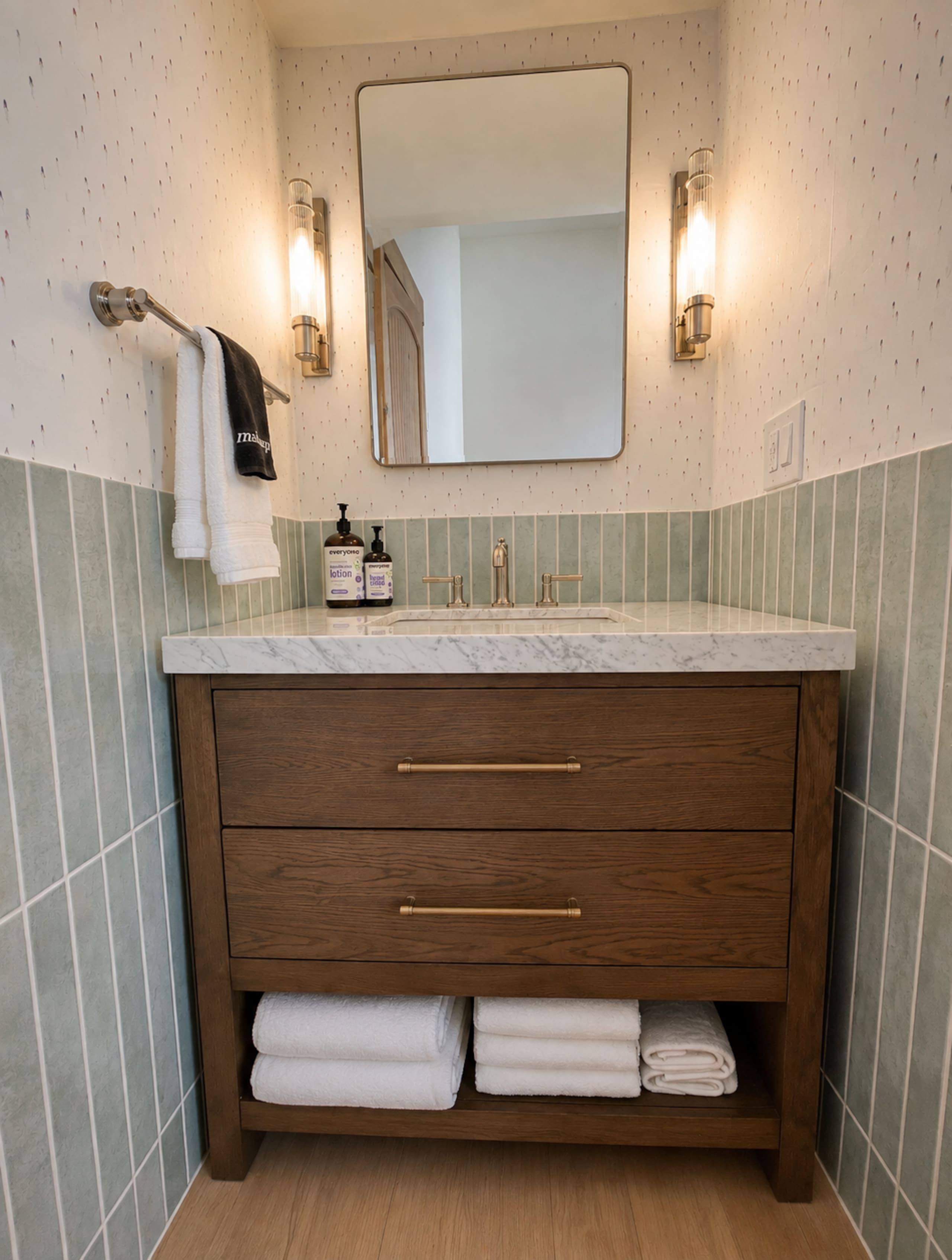 A bathroom with a marble countertop, wooden vanity, two towel racks, and wall-mounted lights.