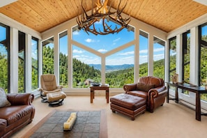 A spacious room with a high ceiling, large windows offering a view of a forested landscape, and leather furniture. - Sky Valley Ranch  (Steamboat Springs)