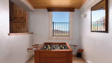 Una habitación con mesa de fútbol, ventana con vistas a colinas y puerta de madera.
