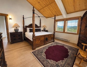 A four-poster bed with a wooden headboard, two bedside tables with lamps, a large patterned rug, and a view of the outdoors through a window. - Sky Valley Ranch  (Steamboat Springs)