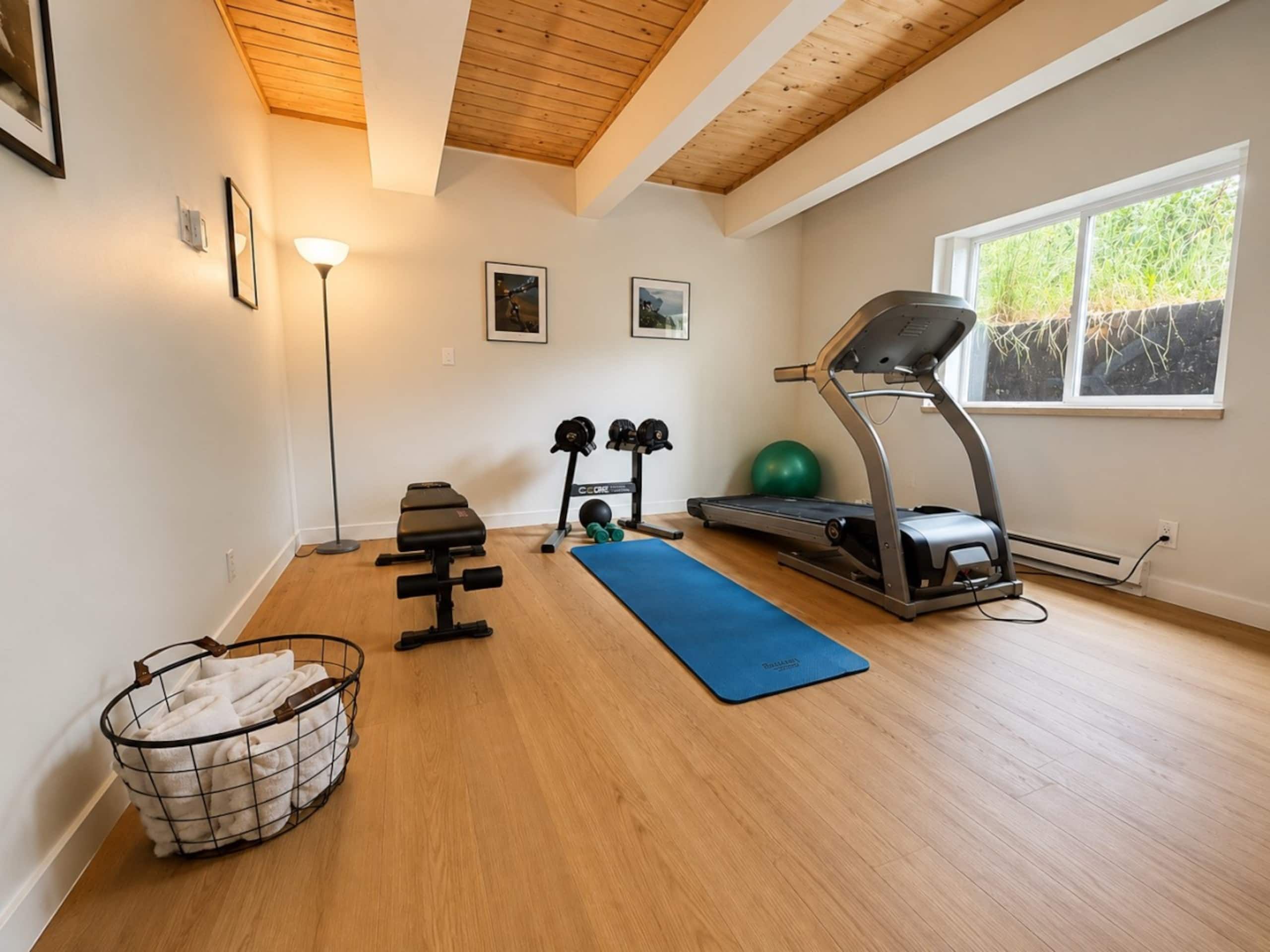 A home gym with a treadmill, weights, and a yoga mat.