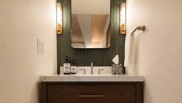Un baño con tocador de madera, un espejo y dos luces fijadas a la pared.