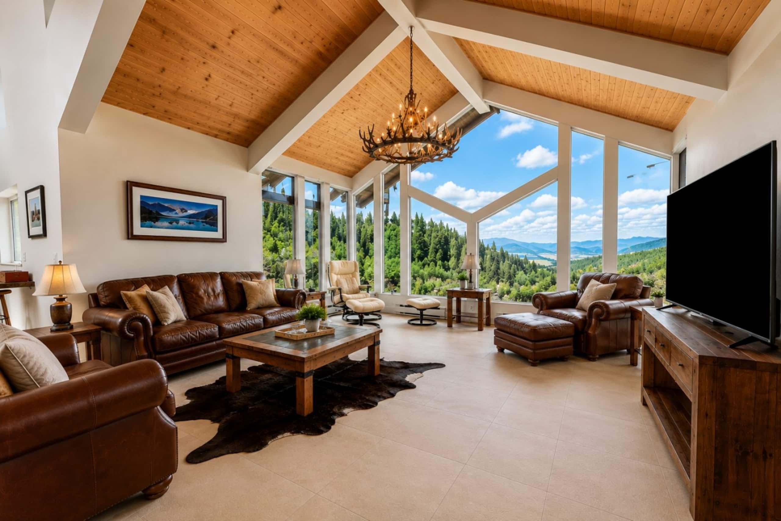 Un salón comedor amplio con techo alto, ventanas grandes con vistas a la montaña, mobiliario de cuero y un televisor de pantalla plana.