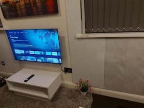 Seinälle asennettu televisio, ja sen alla valkoisella jalustalla kaukosäädin.