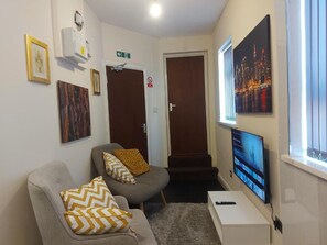 A living room with a grey sofa, a TV mounted on the wall, and a painting of a cityscape.