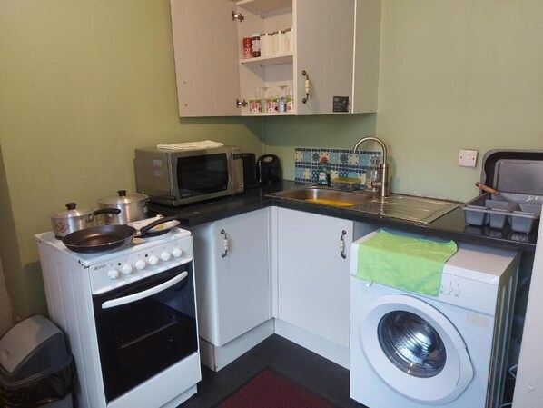A compact kitchen with a stove, microwave, sink, and a washing machine.