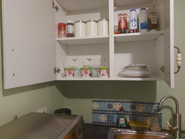 A kitchen with a tiled backsplash, a stainless steel sink, and a cabinet with various food items and kitchenware.