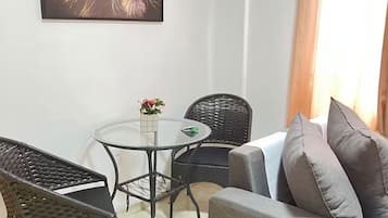 A room with a grey sofa, a black woven chair, a glass table, and a framed picture on the wall.