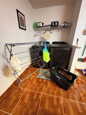 A laundry area with a drying rack, a washing machine, a dryer, and a basket on the floor. - Charming residence with a private pool located in proximity to Disney World (Kissimmee)