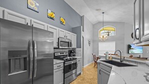 A modern kitchen with stainless steel appliances, a marble countertop, and a view of the outdoors through a window. - Charming residence with a private pool located in proximity to Disney World (Kissimmee)