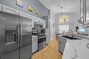 A modern kitchen with stainless steel appliances, a marble countertop, and a view of the outdoors through a window. - Charming residence with a private pool located in proximity to Disney World (Kissimmee)