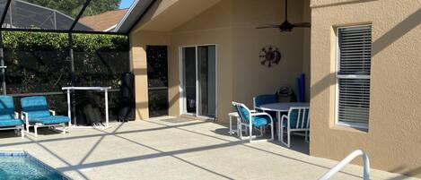 A swimming pool with a glass ceiling, lounge chairs, and a patio area with a ceiling fan.