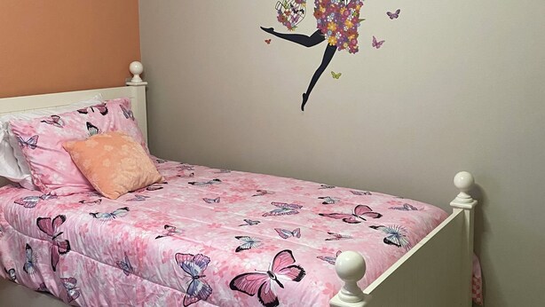 A child's bedroom with a bed, a wall decal of a dancing girl with butterflies, and a pink butterfly-patterned bedspread. - Charming residence with a private pool located in proximity to Disney World (Kissimmee)