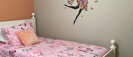 A child's bedroom with a bed, a wall decal of a dancing girl with butterflies, and a pink butterfly-patterned bedspread.