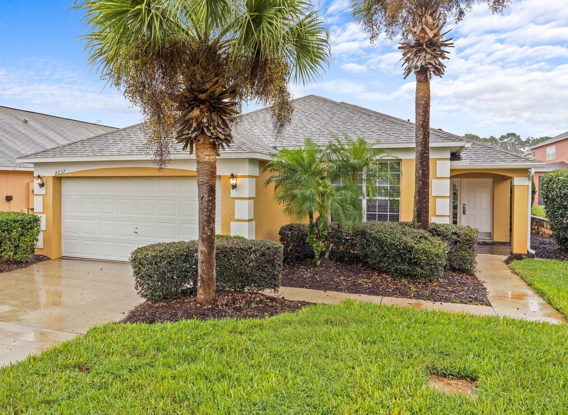 A residential house with a garage, palm trees, and a well-maintained lawn.