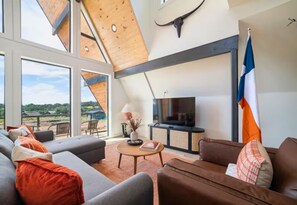 Ein modernes Wohnzimmer mit großem Fernseher, bequemen Sitzmöglichkeiten und Blick ins Freie.