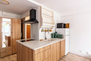 A modern kitchen with wooden cabinets, a built-in microwave, and a coffee maker. - Studio Baignol - Welkeys (Ciboure)