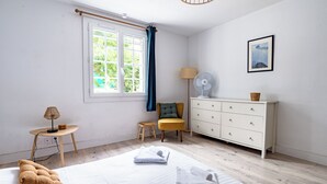 Une chambre à coucher comprenant un lit, une table de chevet avec une lampe, une commode, une chaise et une fenêtre avec des rideaux.