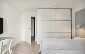 Ein Schlafzimmer mit Bett, Schreibtisch, Stuhl, Kleiderschrank und einer Wandlampe.