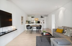 Ein modernes Wohnzimmer mit Flachbildfernseher, Essbereich mit Tisch und Stühlen sowie einer Couch mit Kissen.