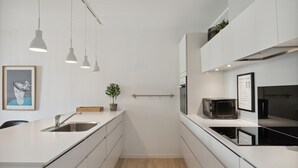 Eine moderne Küche mit weißen Schränken, einer Holzausziehtafel, einer Spüle, einem Topfpflanzen, Pendelleuchten und einer Mikrowelle.