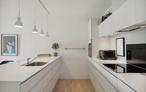 Eine moderne Küche mit weißen Schränken, einer Holzausziehtafel, einer Spüle, einem Topfpflanzen, Pendelleuchten und einer Mikrowelle.