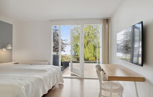 A bedroom with a bed, a desk, and a chair. There is a large window with a view of trees and a building.