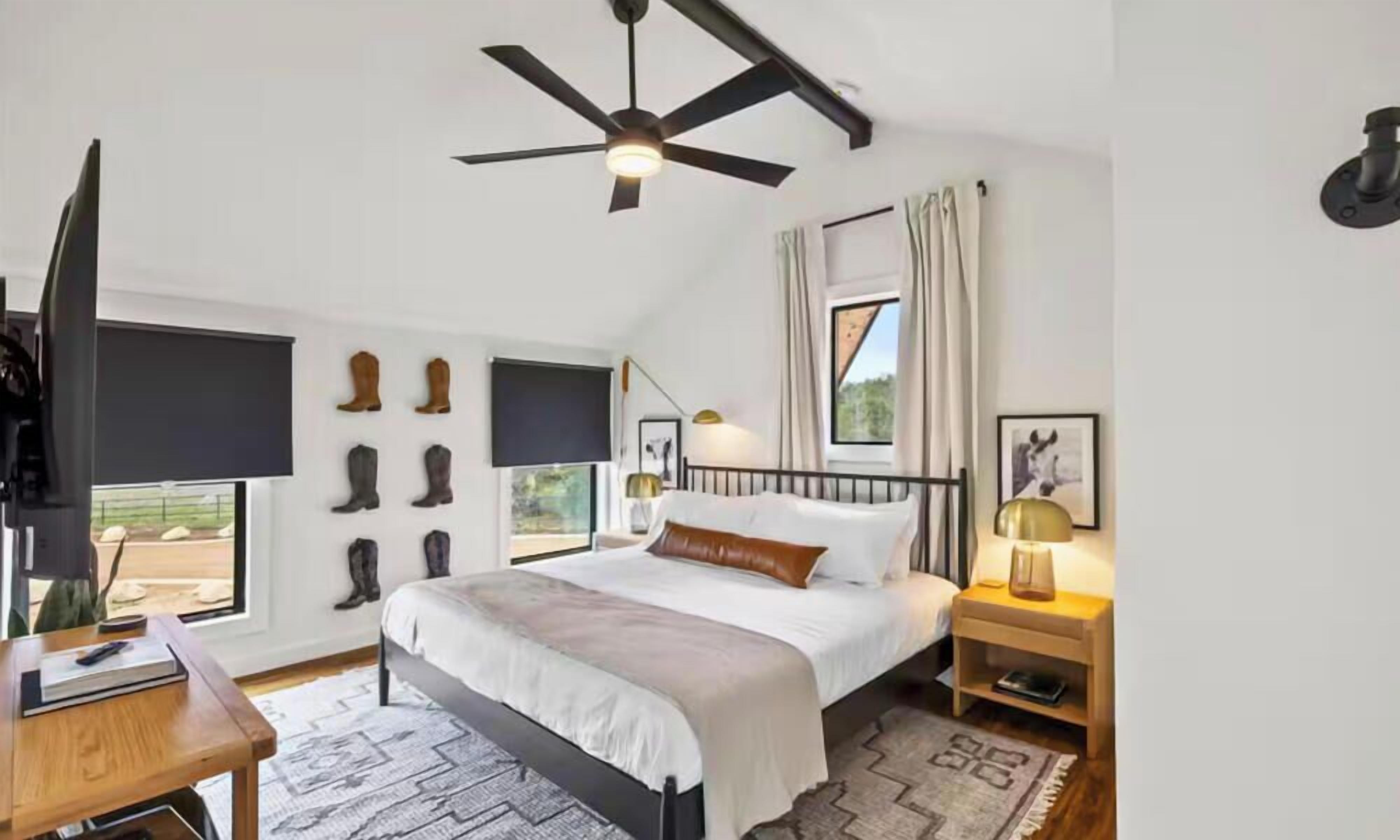 Una camera da letto con un letto, comodini, una ventola a soffitto e una finestra con tende.