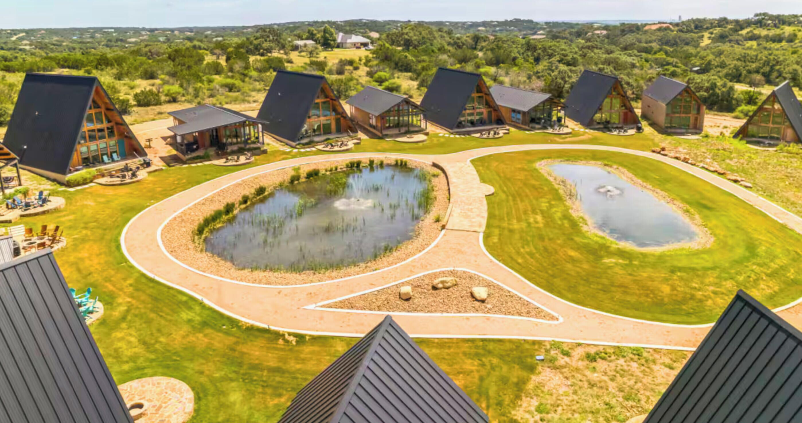 A modern resort with multiple cabins, a central pond, and a well-maintained lawn.