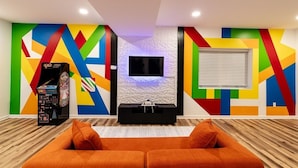 Uma sala de estar moderna com um design geométrico colorido na parede, uma TV de tela plana e piso de madeira.
