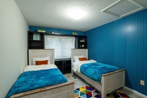 A bedroom with two beds, a window with blinds, a shelf with decorative items, and a blue patterned wall. - 5BR Mass Resort | Movie Lounge +Pool/Poker Table+Arcade+Gym+Remote Workstatio... (McGaheysville)
