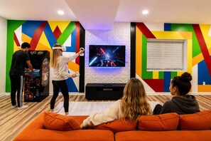 Ein Zimmer mit einem großen Flachbildfernseher, einem farbenfrohen geometrischen Wanddesign und einer Spielkonsole.